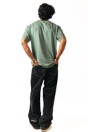 Sollzz शैतान : Inverted Truth Oversize oversize Tee in pastel green, back view of a male model with red graphic detail on the sleeve cuffs, styled with black jeans and beige sneakers