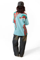 Sollzz Umbra SeaJet Oversize Tee in light blue, back view featuring red and teal graphic mask print, styled with dark washed jeans and a gray cap