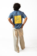 Sollzz Noctra - Silent Watcher Oversize Tee in dark navy blue, back view of a male model featuring a large square yellow patch print with abstract line art artwork, styled with beige wide-leg pants
