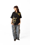 Sollzz Primordia Oversize Tee in black featuring a front view of a female model wearing gold and white abstract face line art graphic prints, styled with baggy washed jeans