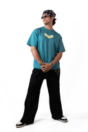 Sollzz - Abyss : Inner Descent Oversize Tee in muted teal, front view of a male model with a yellow minimalist graphic print on the collar and chest, styled with black pants, a black bandana, and sunglasses