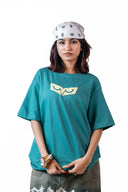 Sollzz - Abyss : Inner Descent Oversize Tee a woman wearing a teal green oversized t-shirt with a cream graphic on the chest, paired with a white paisley bandana and gray pants, photographed against a solid white background.